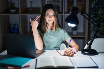 Teenager girl doing homework at home late at night shooting and killing oneself pointing hand and fingers to head like gun, suicide gesture.