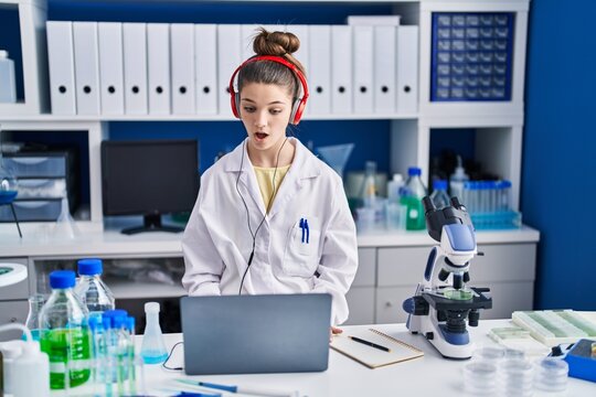 Teenager girl working at scientist laboratory scared and amazed with open mouth for surprise, disbelief face