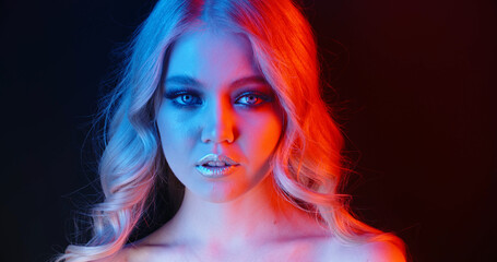 Art beauty. Portrait of a blondine woman with big beautiful blue eyes and long light hair in blue and crimson light. Make-up and cosmetics. 