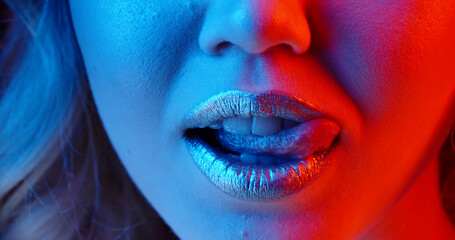 Sensual girl with bright glowing lipstick seductively licking her lips in neon light - nightlife, nightclub concept extreme close up shot  - obrazy, fototapety, plakaty