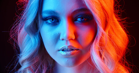 Closeup shot of face of girl wearing glowing makeup doing a seductive growl in neon light - nightlife concept 