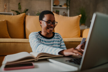 African american woman using credit card and a laptop while online shopping at home