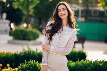 Fashion portrait of a cheerful boho brunette posing in a city park on a sunny summer day while smiling at the camera.