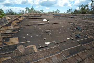 Wind damaged house roof with missing asphalt shingles after hurricane Ian in Florida. Repair of...