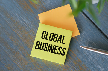 Global Business text on yellow paper on wooden background.