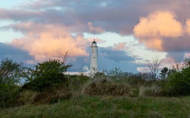 Gordijnen A white lighthouse in front of orange sunrise clouds at the European Wadden island 'Schiermonnikoog' in Friesland, Holland © Daniel Doorakkers