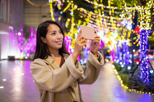 Woman use cellphone to take photo with Christmas light decoration
