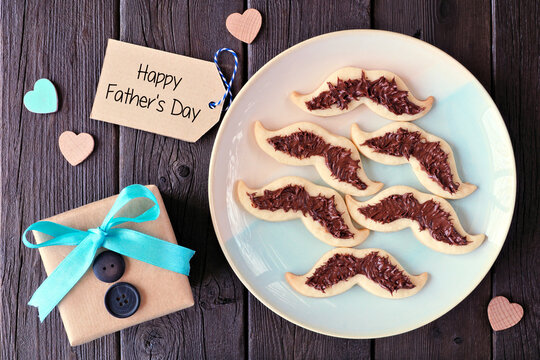 Fun Fathers Day mustache cookies. Top down view with gift greeting card over a dark wood background.