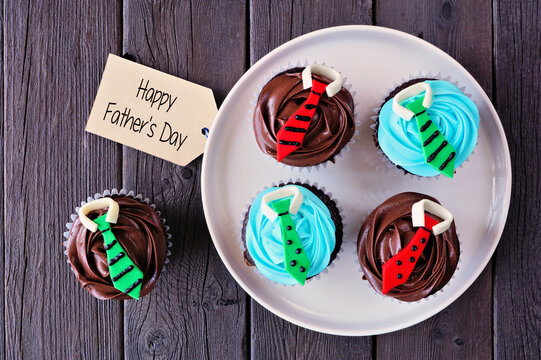 Fun Fathers Day shirt and tie cupcakes. Top down view with gift tag over a dark wood background.