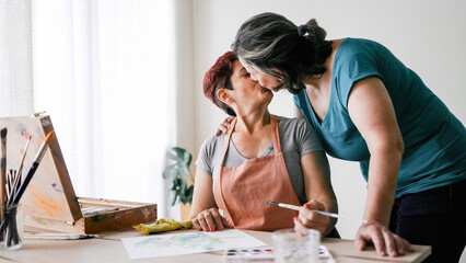 Fototapeta na wymiar Senior artist gay couple painting watercolor canvas at art home workshop - LGBTQ Lesbian mature women kissing - Small family business concept