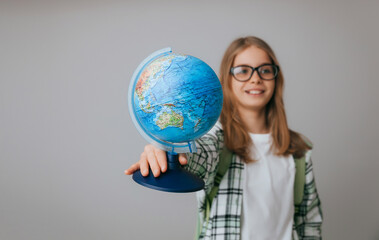 Caucasian young teenager schoolgirl student holding a globe on a gray background, isolated. Happy earth day