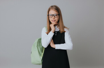 cheerful teenage girl 11,12,13 years old in a school uniform wears a backpack on a gray background....
