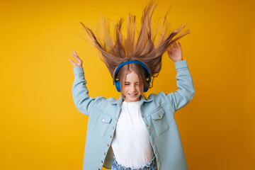 A young girl 11-13 years old in headphones listens to music and dances in the studio on a yellow background