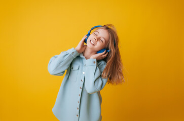 A young girl 11-13 years old in headphones listens to music and dances in the studio on a yellow background