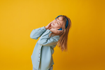 A young girl 11-13 years old in headphones listens to music and dances in the studio on a yellow background