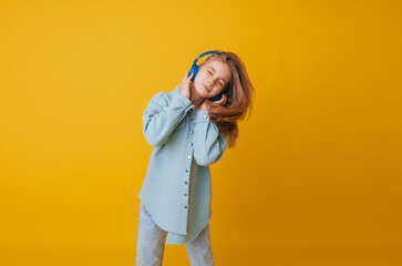 A young girl 11-13 years old in headphones listens to music and dances in the studio on a yellow background