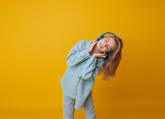 A young girl 11-13 years old in headphones listens to music and dances in the studio on a yellow background