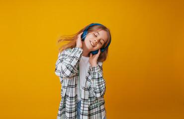 A young girl 11-13 years old in headphones listens to music and dances in the studio on a yellow background