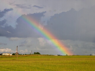 Rainbow on a cloudy field against a green field.