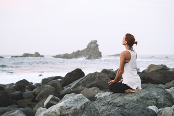 Woman is practicing yoga, meditating on the beach.