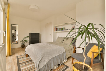 a bedroom with a bed, chair and plant in the corner on the right side of the room is white