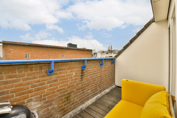 a balcony with yellow couches and blue pipes on the wall in front of a white brick building, against a bright blue sky