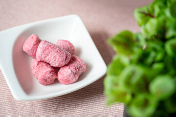 Still frozen pink (beetroot) gnocchi in a white small bowl on the pink cloth. Baby swiss chard in the backgrond.