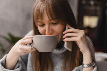 Blonde woman smiling positive conversation talking to her friend using phone hand hold hot drink tea relax casual positive emotion weekend relax routine at cafe restaurant. Girl have discussion.