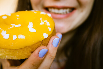 A young woman girl holding a glazed icing yummy yellow doughnut in her hand. Calories, fast food, glazed sweets, baked goods and treats. Eating junk food. Happy girl shows a golden mango donut.