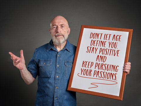 Do not let age define you. Stay positive and keep persuing your passions. Message on a whiteboard held by a happy and confident senior man.