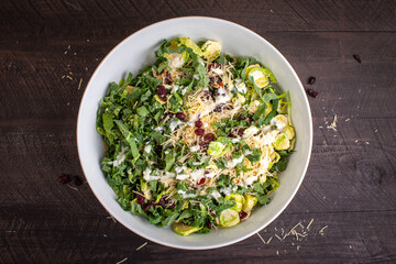 Kale and Shaved Brussels Sprouts Salad topped with dried cranberries, grated fresh parmesan cheese,...