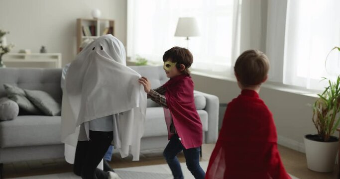 Cheerful Grandpa Watching Preschool Boy Friends Playing Active Funny Role Games At Home, Wearing Superhero, Ghost Homemade Costumes, Running, Chasing Each Other, Enjoying Activity, Entertainment