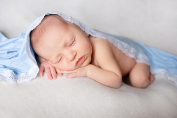 newborn baby sleeps on a white blanket under a blue blanket. Healthy newborn child take a nap asleep. Closeup portrait of  happy baby sleeping sweet dream on bed