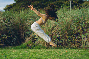 latin woman dancer in nature jumps with her arms backwards and her legs forwards