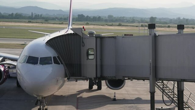 Skopje, Macedonia - 26 Jun, 2022: Passengers disembark from plane docked with boarding bridge, slow motion