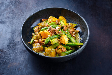 Traditional curry chicken fillet with orange, green asparagus and nuts in sweet sour vinaigrette served as a close-up in a design plate with text space