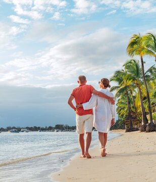 Couple in love hugging while walking on a sandy exotic beach. They have an evening walk by Trou-aux-Biches seashore on Mauritius island. People relationship and tropic honeymoon vacations concept