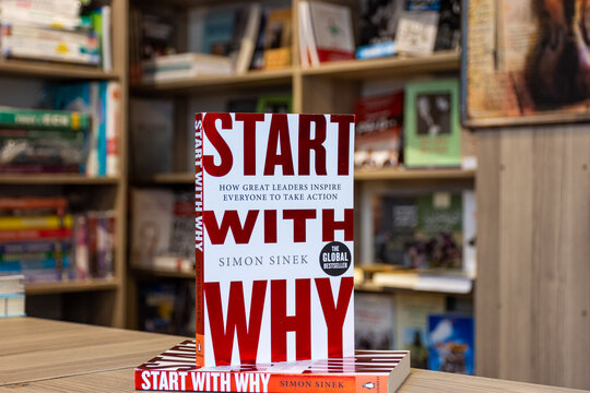 Close-up view of the bestselling book "Start With Why" by Simon Sinek displayed on a wooden table in a bookstore with blurred bookshelves in the background.