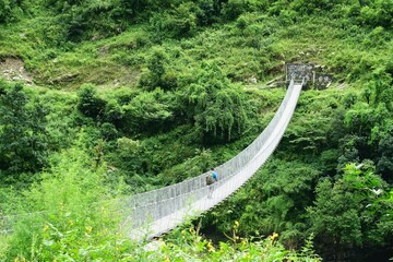 A suspension bridge, which adds to the natural beauty of a tranquil rainforest rich with lush foliage and growth in the Himalayas, can be viewed from a high angle on the Manaslu Circuit trek in Nepal.