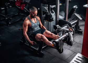 Fototapeta na wymiar Man in gym training at weights machine to define his leg muscles