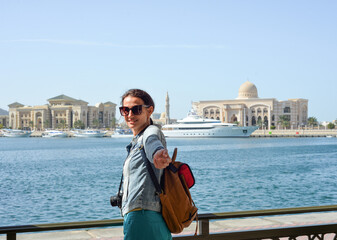 A young woman tourist with a backpack looks at the administrative region of the emirate of Sharjah with the port and ships.