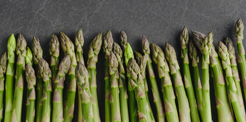 Line of fresh green asparagus on stone dark background, top view. Banner, copy space