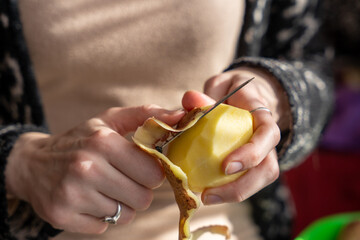 Close up of women holding and peeling potato with a knife