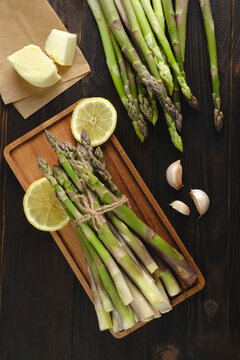 Brunches of healthy green asparagus on wooden background with salt garlic and lemon, top view. Cooking process ingredients
