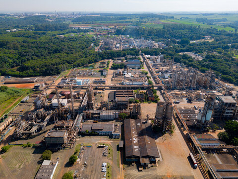 Aerial image of chemical industry. Large structure of pipelines and warehouses with movement of cargo trucks. Industry surrounded by vast vegetation and trees. Located in Brazil, city of Paulínia.