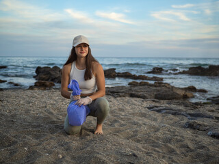 Smiling volunteer woman looking at the horizon collecting plastic in a blue plastic bag to clean the beach, Concept of ecology and World Environment Day, Concept of saving the earth.