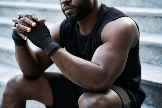 Fit confident sporty young black man boxer fighter sitting outdoors. Strong African ethnic guy relaxing after street workout exercises or boxing, resting after training outside. Close up