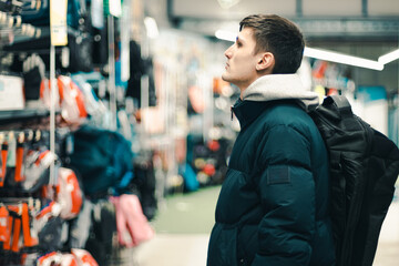 A young guy chooses a backpack in a store.