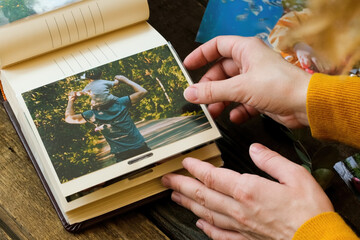 Photo printing concept. Female hands adding printed photo to picture album. - obrazy, fototapety, plakaty