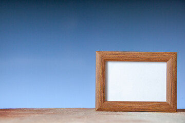 Close up view of brown empty picture frame standing on table on the left side on blue wave background